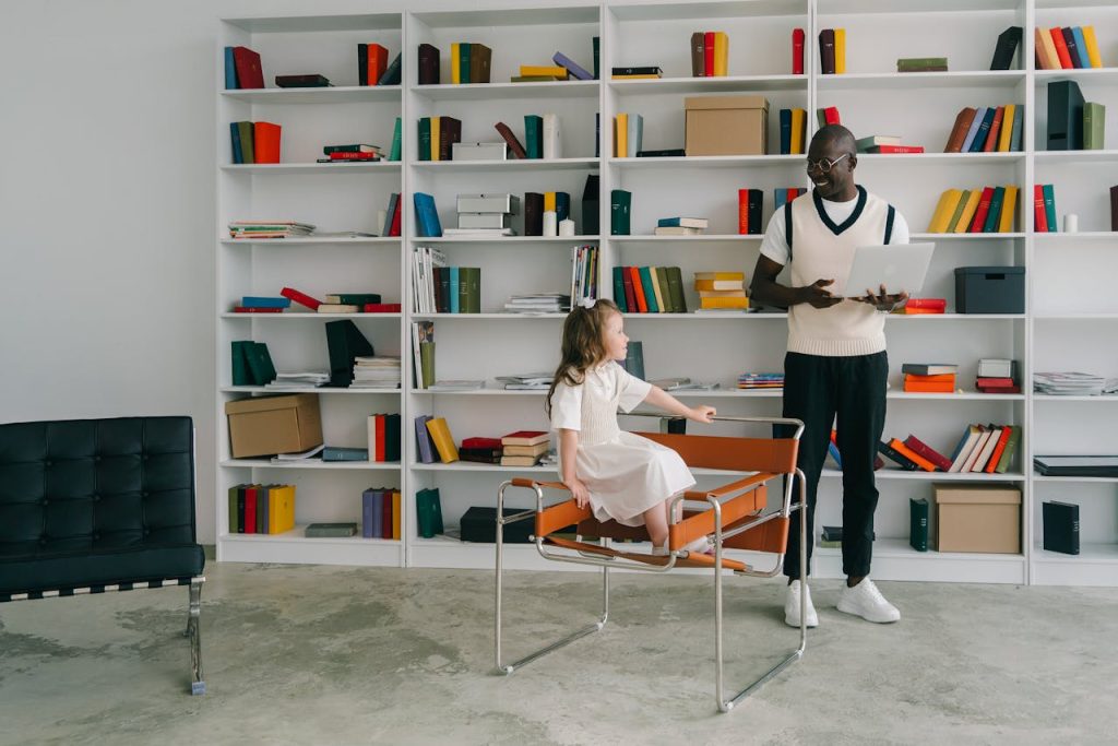 A man tutors a young girl in a well-organized modern library, fostering education and diversity.