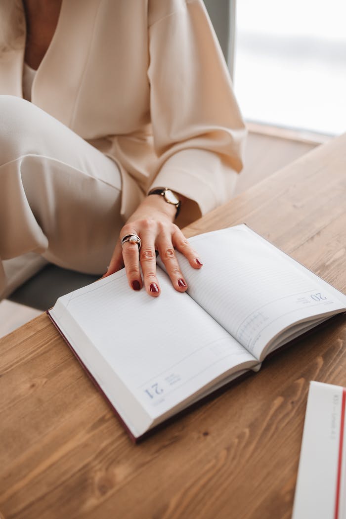 Close-up of a womans hand on an open diary on a wooden table, capturing an intimate reading moment indoors.